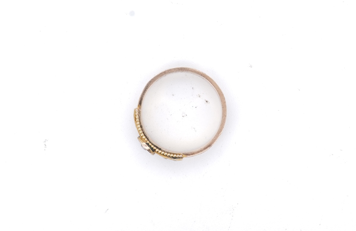 A George V 9ct gold, black enamel and seed pearl set mourning ring, the shank with panels of plaited hair, size O, gross weight 2.5 grams.
